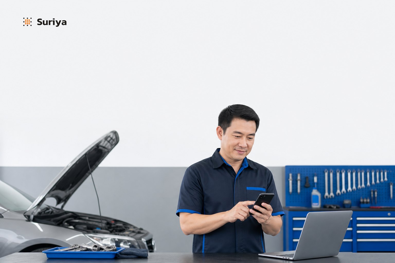 Thai mechanic in a busy auto repair shop checking customer booking messages on a smartphone